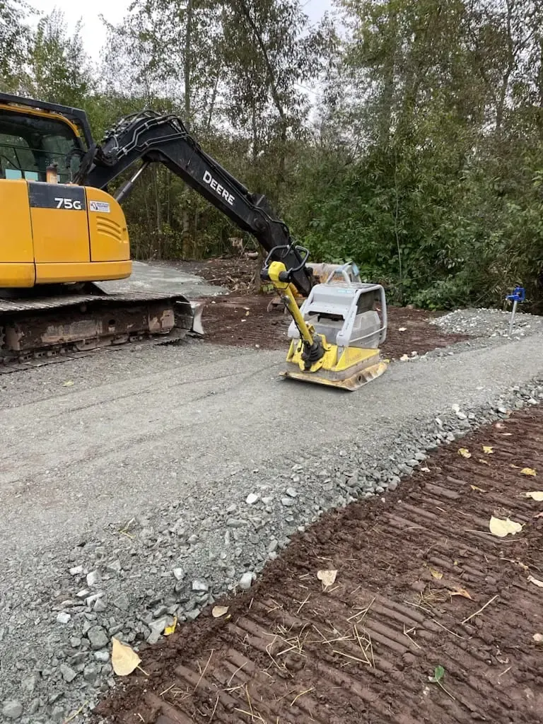 An excavator and plate compactor working a gravel base
