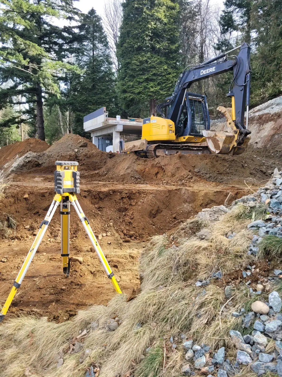 An excavator and surveying tripod on a Fraser Valley job site