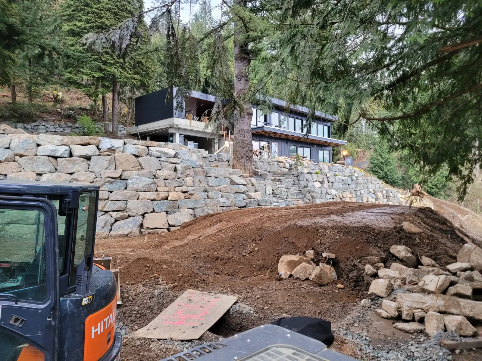 A rock retaining wall being rebuilt beside a house