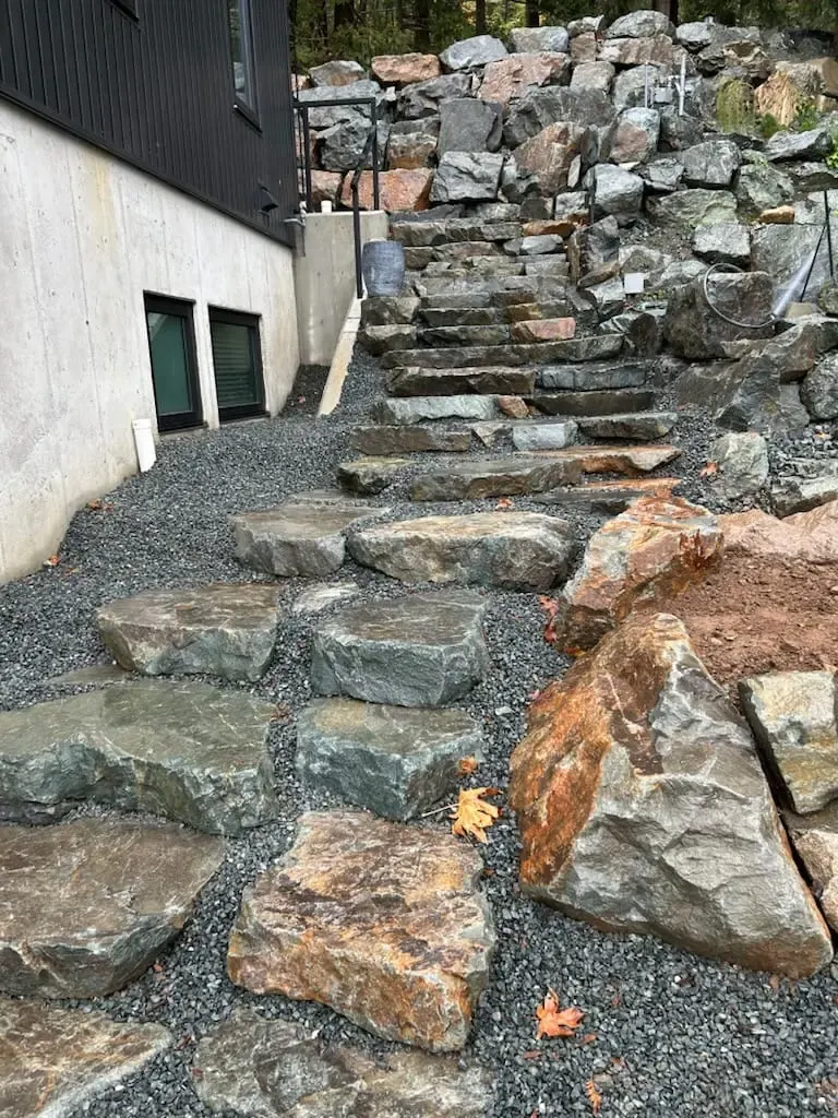 A rock retaining wall with stone steps set into the face