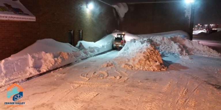 Commercial snow removal in Chilliwack – Fraser Valley Contracting Bobcat clearing large snow piles in a commercial parking lot at night